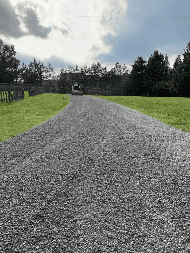 Fonvilletreeservice crew operating skid steer to grade fresh gray gravel driveway between green lawns in NC