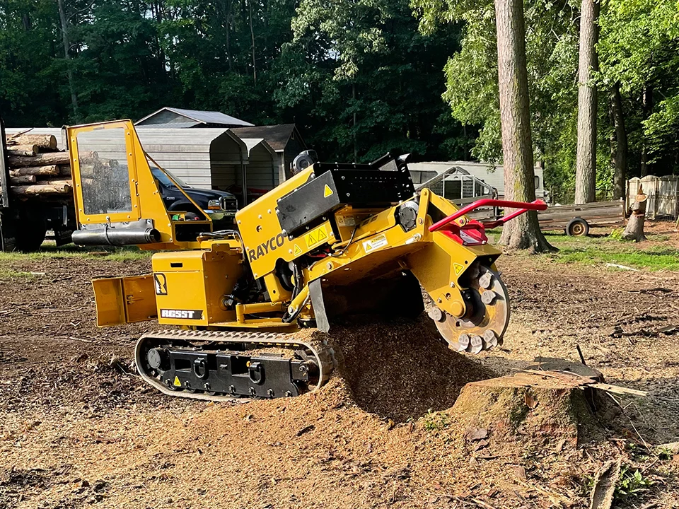 Fonvilletreeservice operates yellow Rayco tracked stump grinder removing large tree stump in residential backyard in NC
