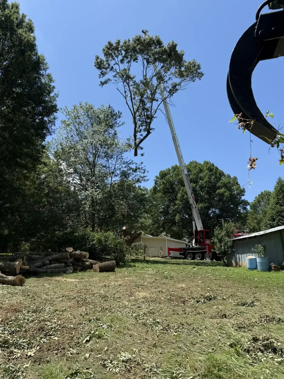Fonvilletreeservice crane lifting tall tree section while grapple equipment manages cut logs at residential property in NC