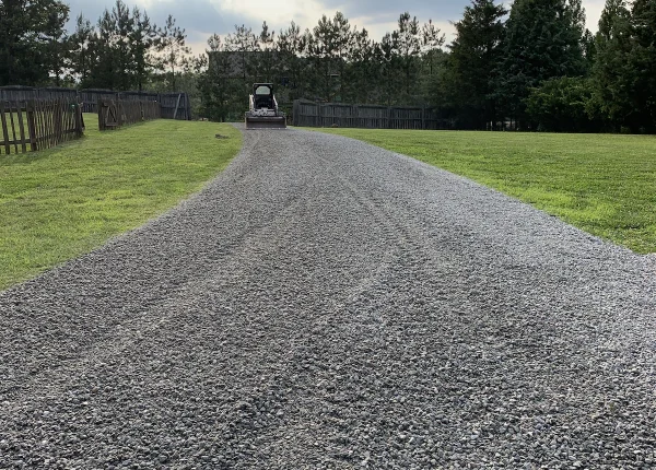 Fonvilletreeservice skid steer operator grading fresh gray gravel driveway through green lawn in residential NC property