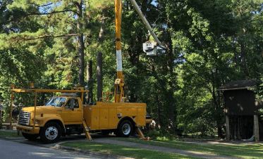 Fonvilletreeservice crew member operating yellow bucket truck to trim tall trees in residential neighborhood in NC.