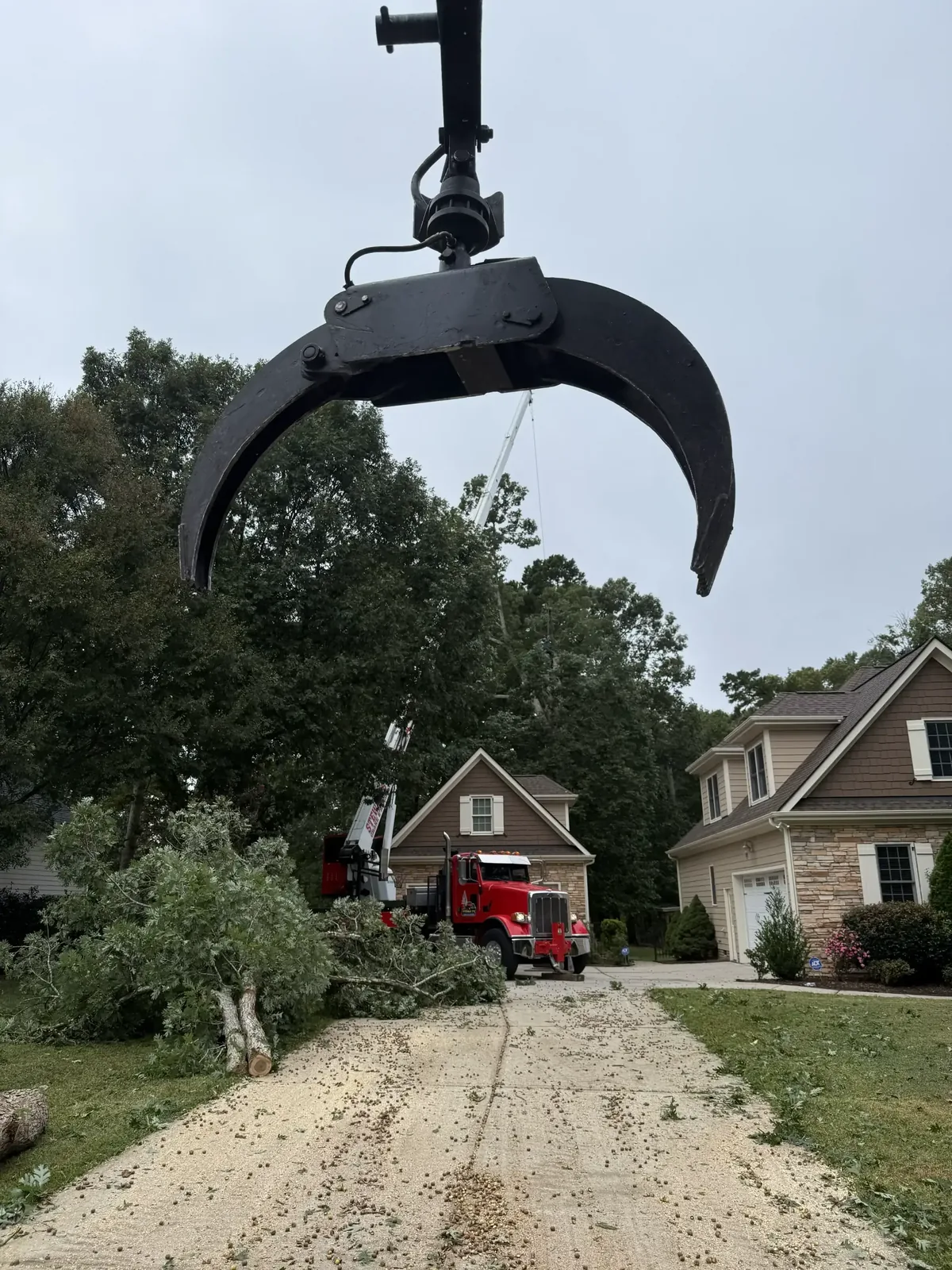 Fonvilletreeservice grapple crane attachment positioned above felled tree sections during residential tree removal operation in NC