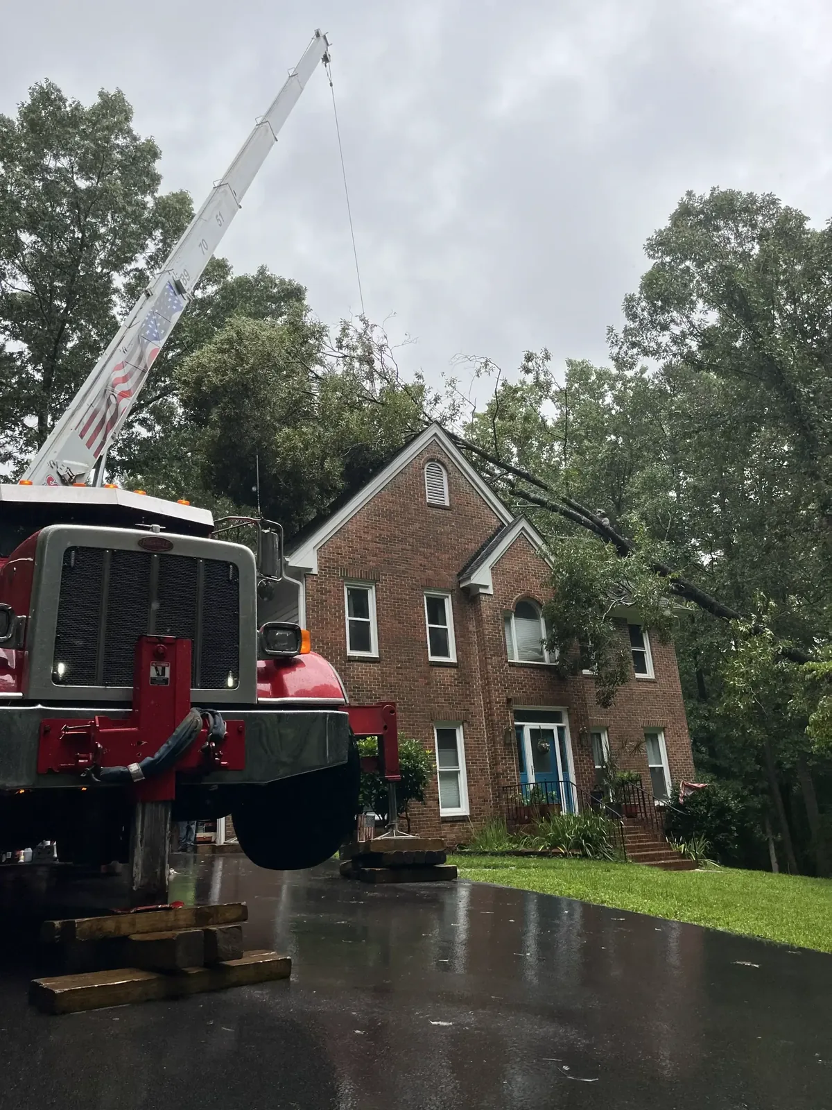 Fonvilletreeservice crane truck removing large fallen tree from residential brick home roof during storm cleanup in NC