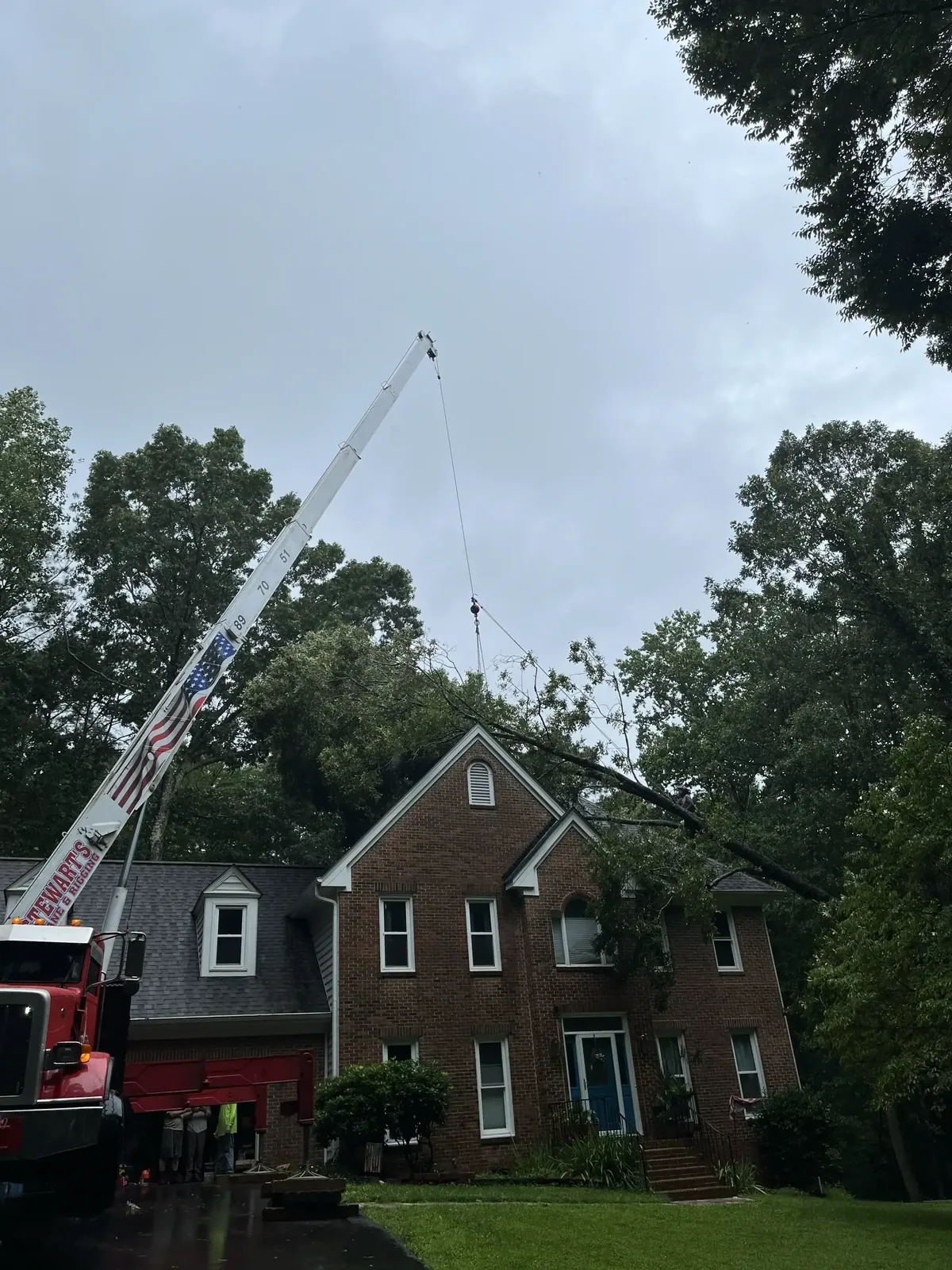 Crane lifting over a brick home during tree removal Crane lifting over a brick home during tree removal